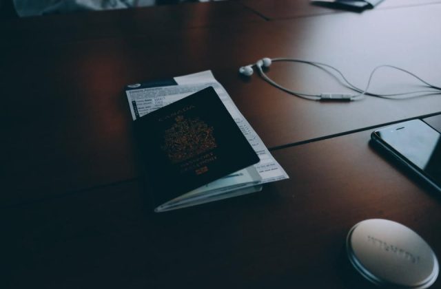 A passport and boarding pass resting on a table with headphones and a phone