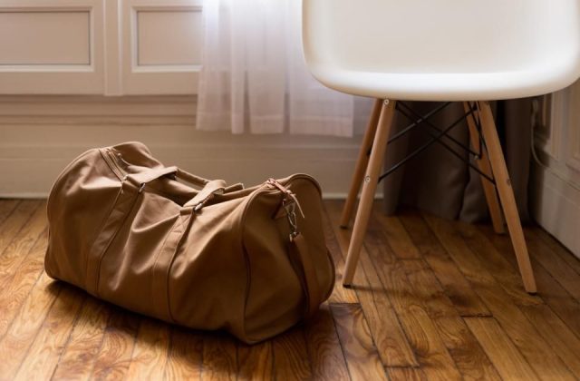 A packed canvas duffel bag on a wooden floor beside a chair