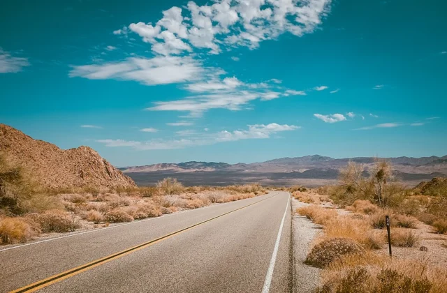 An empty desert highway stretching to the horizon with mountains in the distance, evoking distance and travel measurement